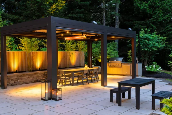 1 - Fireplace Gallery Outdoor covered dining pavilion with a table and chairs, warm lighting, lanterns, and a built-in grill in a landscaped backyard.