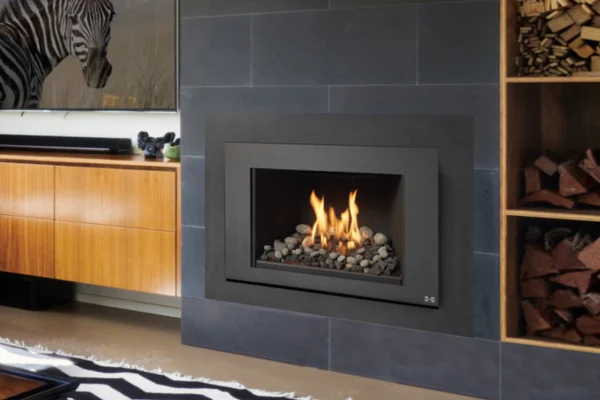 Modern living room with a square-framed fireplace set into a dark slate wall, burning with rocks inside, wood storage on the right.